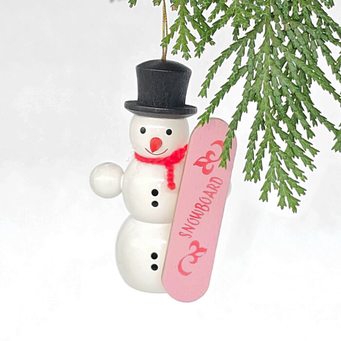 kleiner weißer Holzschneemann hängend mit pinkem Snowboard